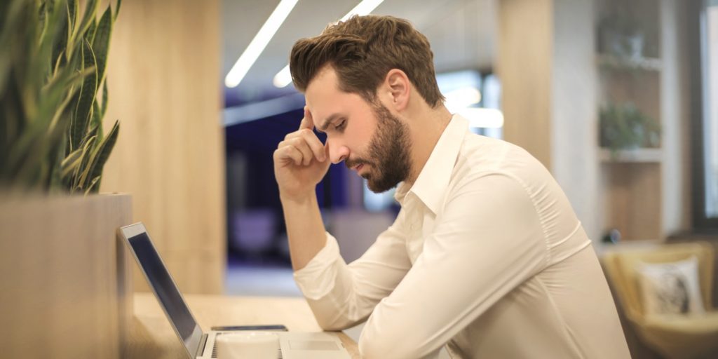 A man sitting before a computer, and has a headache