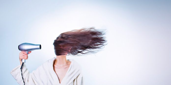 A woman holding a hair drier, and wearing a bathroom robe